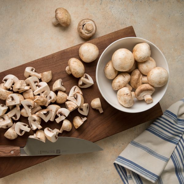 Quartered and whole mushrooms on a cutting board.