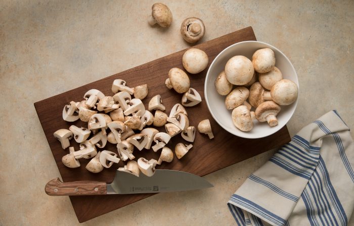Quartered and whole mushrooms on a cutting board.