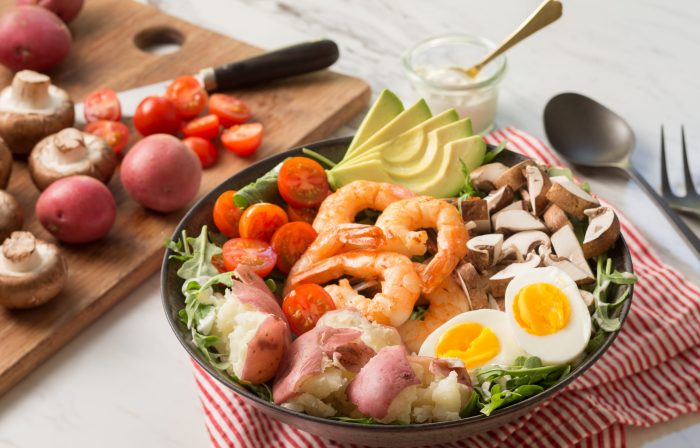 Bowl of shrimp cobb salad next to cutting board of vegetables.