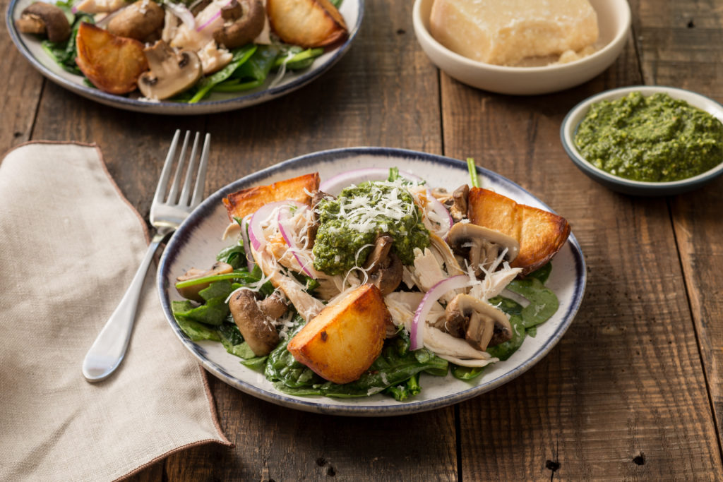 Plate of wilted spinach salad with chicken, potatoes, mushrooms, pesto and Parmesan cheese.