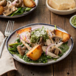Plate of wilted spinach salad with chicken, potatoes, mushrooms, pesto and Parmesan cheese.