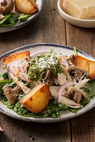 Plate of wilted spinach salad with chicken, potatoes, mushrooms, pesto and Parmesan cheese.
