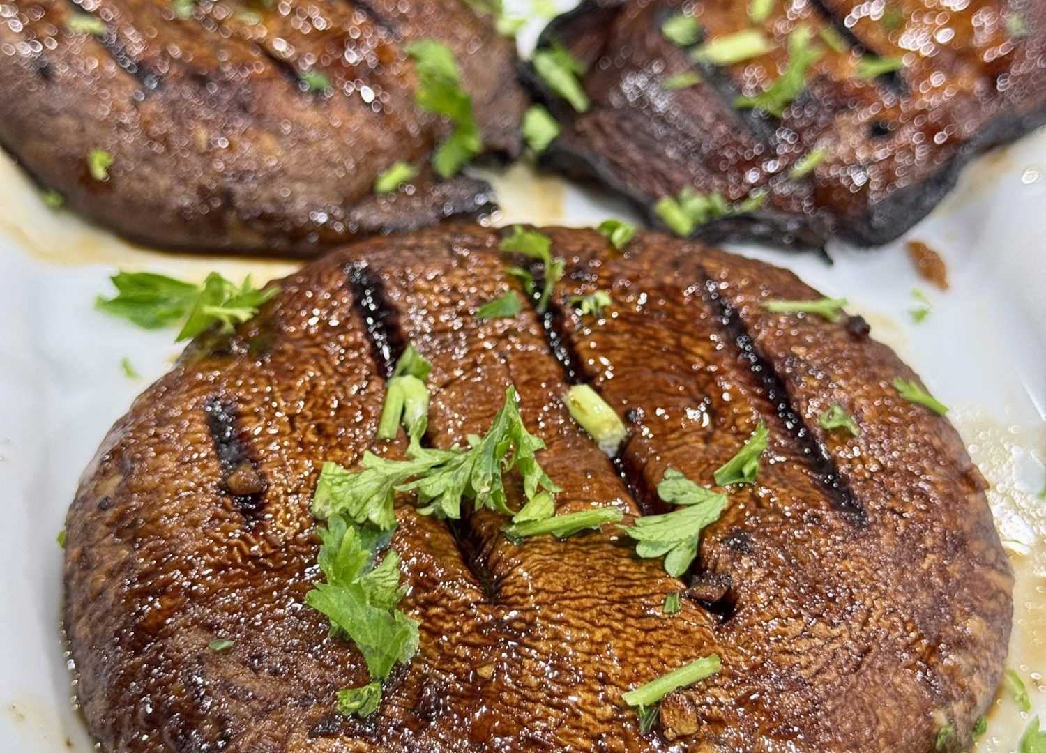 Grilled portabella mushrooms, glazed and garnished with parsley, on a white platter.
