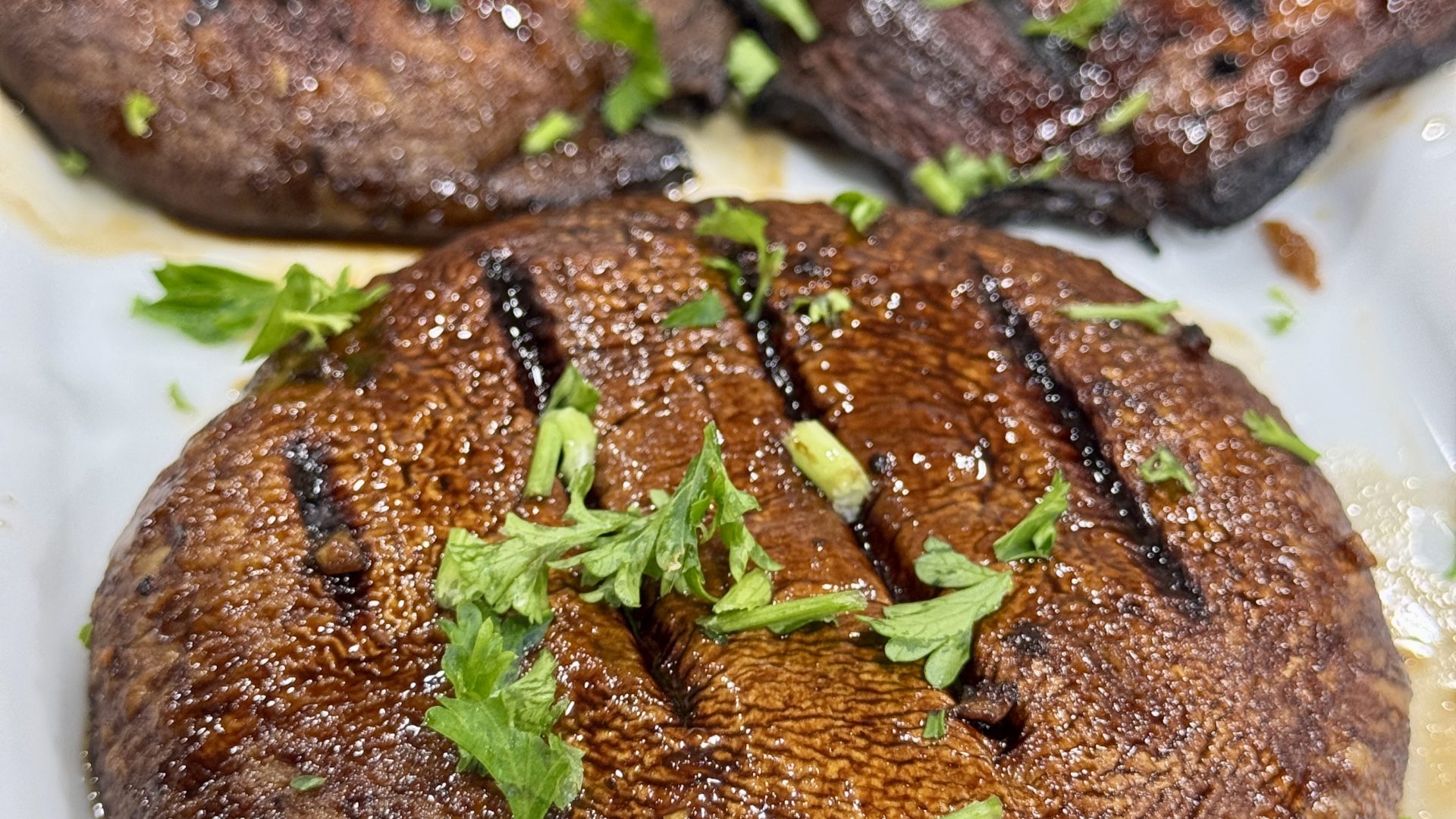 Grilled portabella mushrooms, glazed and garnished with parsley, on a white platter.