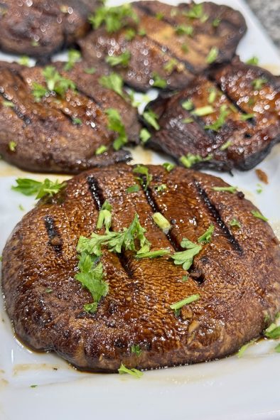 Grilled portabella mushrooms, glazed and garnished with parsley, on a white platter.