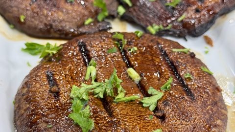 Grilled portabella mushrooms, glazed and garnished with parsley, on a white platter.